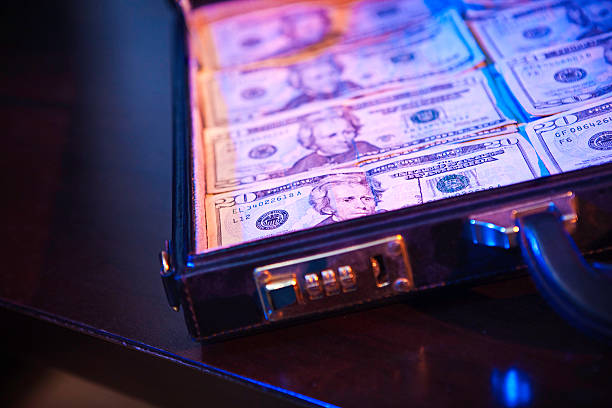 Stacks of Money In A Briefcase Twenty dollar bills lay in an open black leather locking brief case.  Dramatic red and blue lighting give a dark contrast effect.  Horizontal with copy space. money laundering stock pictures, royalty-free photos & images