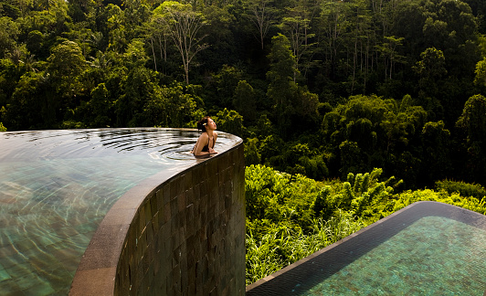 Beautiful setting of a woman leaning over one of two infinity pools at an exotic locale in Ubud, Bali.