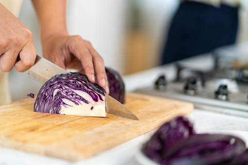 Asian man hand using knife cutting fresh red cabbage on cutting board in the kitchen at home. Happy guy enjoy cooking and having dinner eating healthy food on holiday vacation.