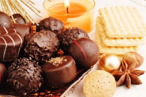 chocolate truffles on a brown plate with chrismas decoration, burning candles, cookies, star anise and golden bauble