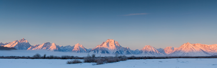 Panorama of Mount Moran and the Teton mountain range in winter with sunrise light  