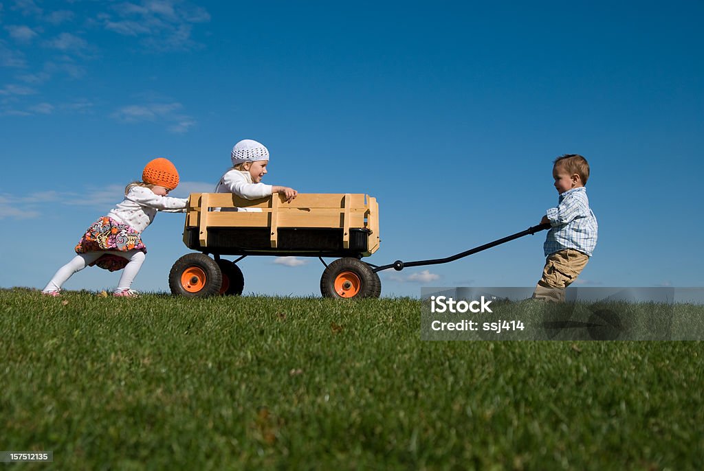 Tre bambini, spingere, tirare e giocare con Wagon - Foto stock royalty-free di Spingere