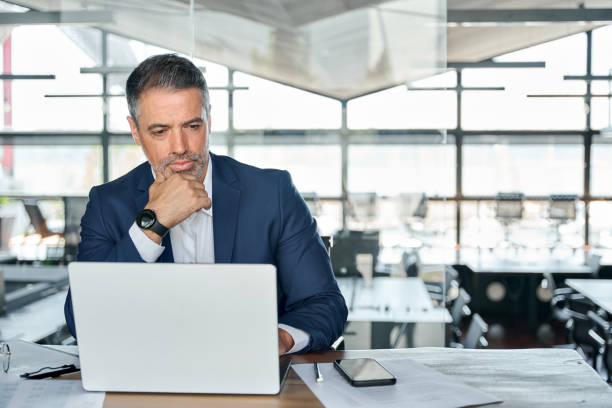 istock Serious mature business man executive sitting at desk using laptop. 1575126016
