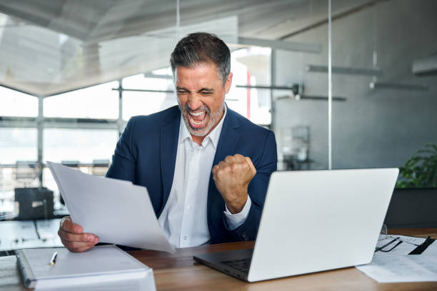 istock Happy middle aged business man holding documents celebrating success in office. 1575126073