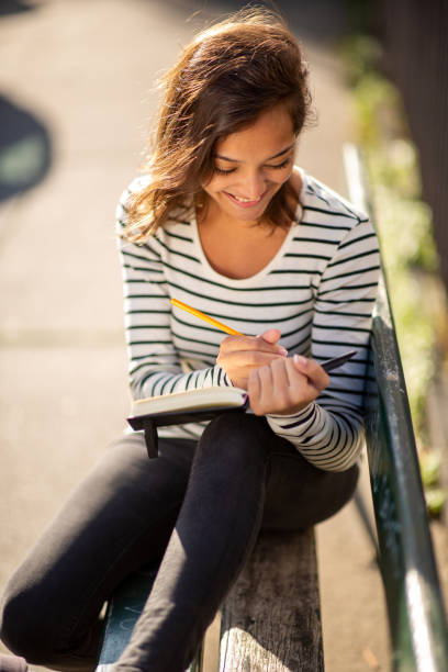 istock happy young woman sitting on bench and writing in book 1575128861