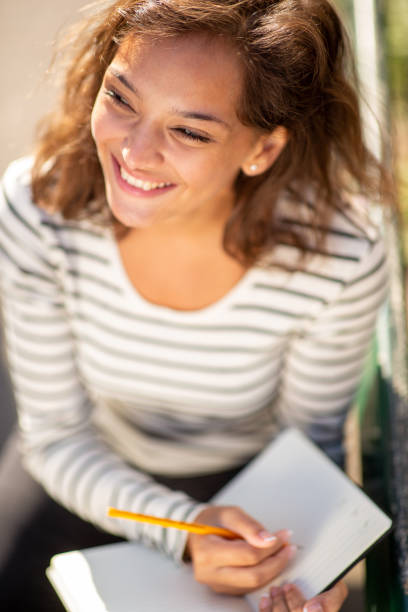 istock smiling young woman writing in journal and looking away 1575128892