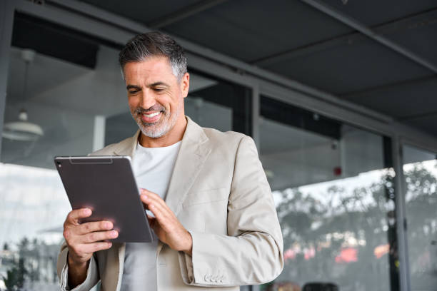Happy mid aged business man standing outside office using digital tablet.