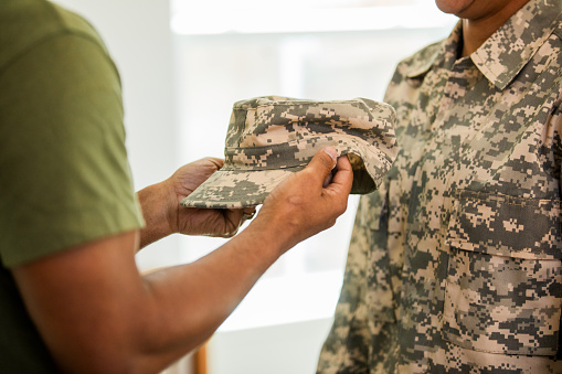 The unrecognizable soldier proudly hands his uniform cap to his colleague.