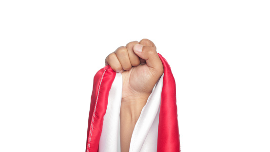 Human hand holding a red and white ribbon as a symbol of the Indonesian flag isolated.