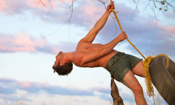 jovem hipster balançar de baloiço de corda ao pôr do sol - men swing tire rope swing imagens e fotografias de stock