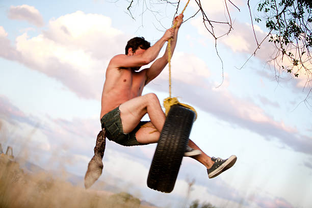 junge hipster schwingen auf seilschaukel bei sonnenuntergang - men swing rope swing tire stock-fotos und bilder