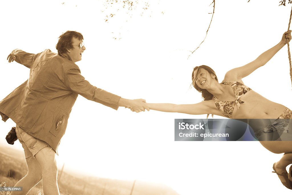 Jovem casal brincando em um balanço de corda ao pôr-do-sol - Foto de stock de 1970-1979 royalty-free
