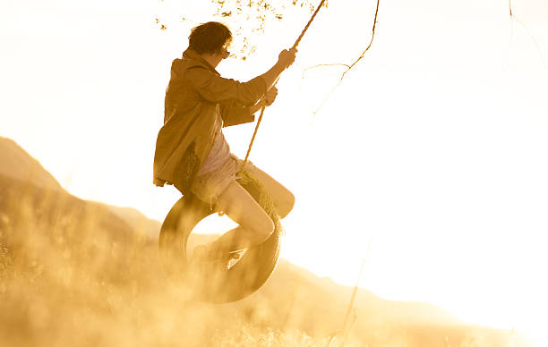 junger mann auf seilschaukel bei sonnenuntergang - men swing rope swing tire stock-fotos und bilder