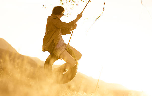 jovem de baloiço de corda ao pôr do sol - men swing tire rope swing imagens e fotografias de stock