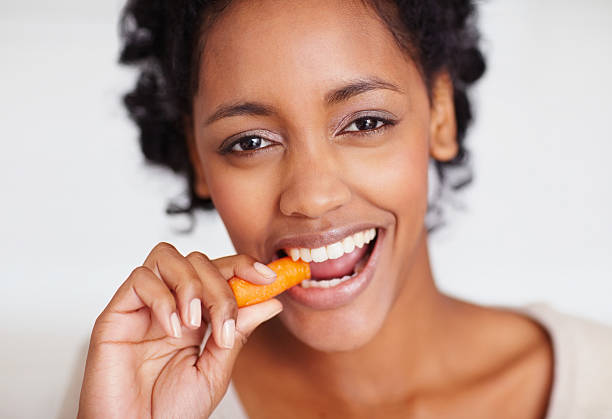 Feliz joven mujer afroamericana comiendo una zanahoria - foto de stock