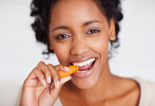 The girl nibbles a carrot. She opens the mouth wide and shows healthy teeth. The concept of healthy eating and veganism. The focus on the carrot