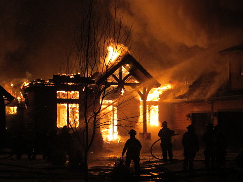 Firemen use a fire hose to try and put out a house fire during a snowfall.