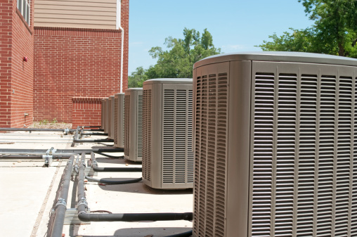 A row of large industrial air conditioners next to an institutional building in the midst of a summer heat wave.