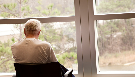 Patient in a hospital enjoying the view in a waiting room.  Senior adult man.