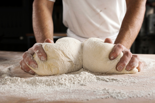A closeup of baker's hands rolling out the bread dough on the table