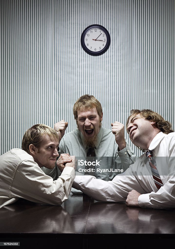 Arm Wrestling Business Team Rival businessmen settle a dispute with an arm wrestling match, another coworker cheering them on.  Vertical with copy space. Mischief Stock Photo
