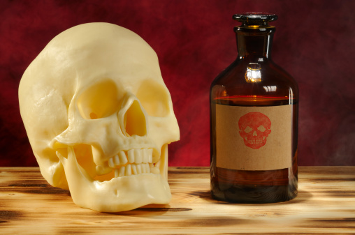 Skull and old chemical bottle is on wooden desk. A label with skull was added.