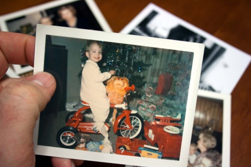 Hand holds Vintage photograph of boy on tricycle at christmas