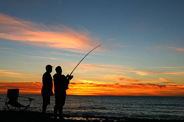 A silhouette of two men fishing at sunset stock photo