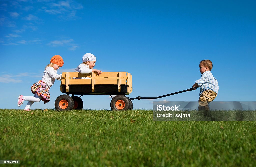 Tre bambini piccoli spingere, tirare e giocare con una carrozza - Foto stock royalty-free di Lavoro di squadra
