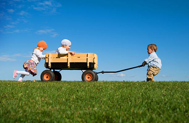 Three Small Children Pushing, Pulling and Playing with Wagon stock photo