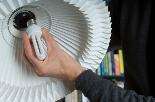 Changing To A  Low Energy Lightbulb. Close up of a man's hand changing the bulb in a floor lamp to a low energy version. Focus on the man's hand as he works. Horizontal format.