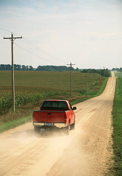 istock Red pickup truck on a dusty road in between fields 157525505