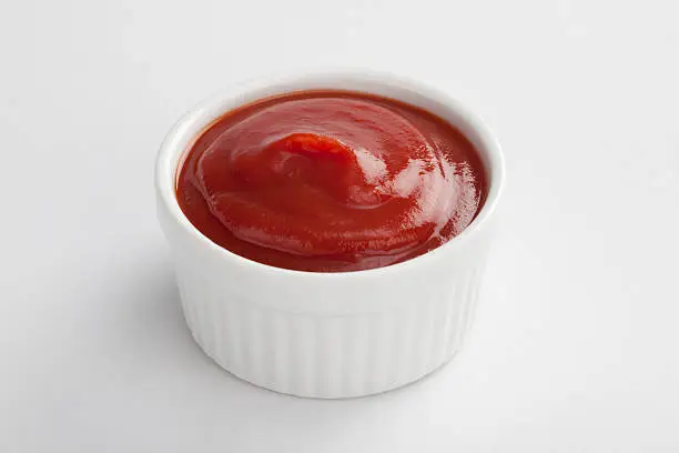 Photo of White dip cup filled with ketchup on white background 