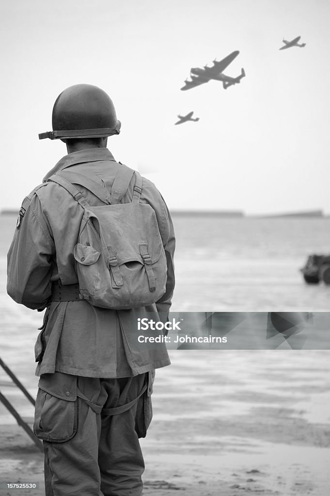 Soldier on  Omaha Beach. WW2 US Soldier looks towards the sky to see fly-past of Two spitfire planes and a Lancaster Bomber.Taken at the 65TH Anniversary of D-Day Normandy.Picture has been aged to give the feel of a vintage  photograph reenactment.  D Day Stock Photo