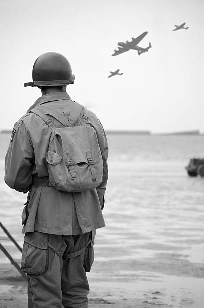 Soldier on  Omaha Beach. WW2 US Soldier looks towards the sky to see fly-past of Two spitfire planes and a Lancaster Bomber.Taken at the 65TH Anniversary of D-Day Normandy.Picture has been aged to give the feel of a vintage  photograph reenactment.  normandy stock pictures, royalty-free photos & images