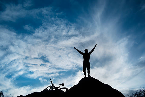 istock silhouette mountain bike man arms raised into sky 157525725