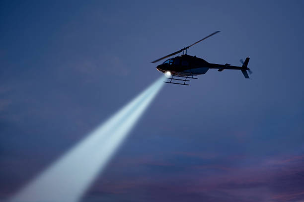 Police helicopter shining a light beam in the dark sky stock photo