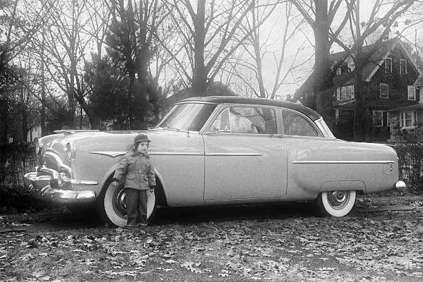 Little boy posing in front of 1953 Packard Coupe. Photographed in 1955. Scanned film with grain.