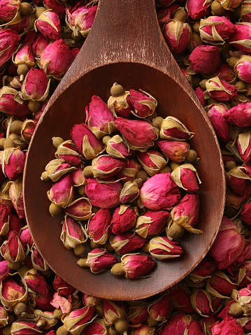 Top view of wooden spoon full of little rose heads for making tea