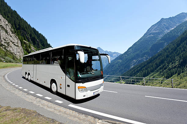 A white coach, or long haul bus for tourists drives through the open roads of Spain, Europe on a summer day. There are white clouds against a blue sky and countryside.