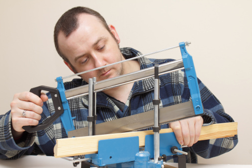 on plain background, a craftsman carpenter adjusts a jig with a tenon saw and some wood moulding for a picture frame