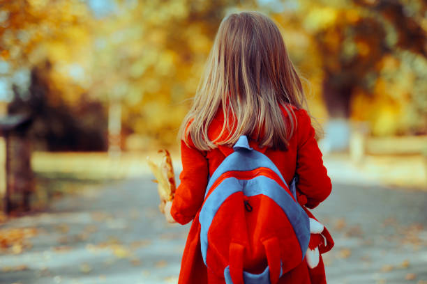 Rear view of male elementary school student walking alone to school while carrying backpack