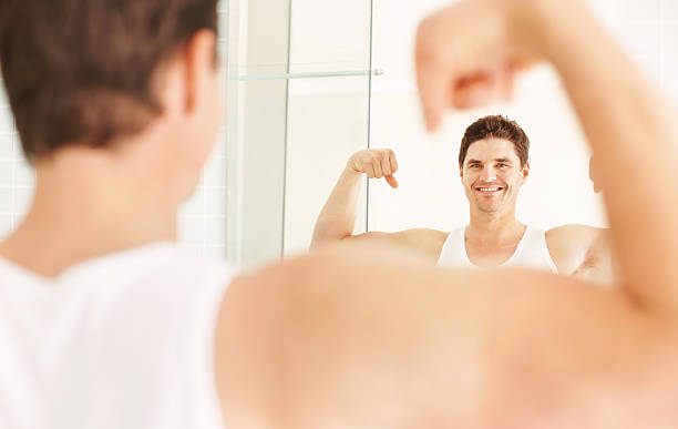 istock Smiling guy showing muscles in front of mirror 157527794