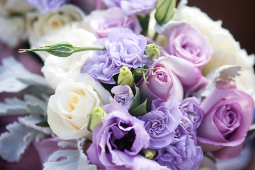 A closeup shot of a vase filled with beautiful pink roses and purple flowers with a white background