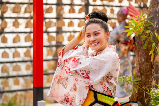 Portrait of pretty young woman wear japanese style dress and hold decoration on her hair also look at camera in front of row of lantern.