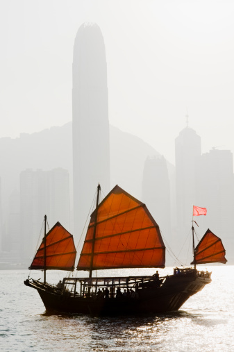 Chinese junk boat in Victoria harbour, Hong Kong, silhouette. City skyline in the background.