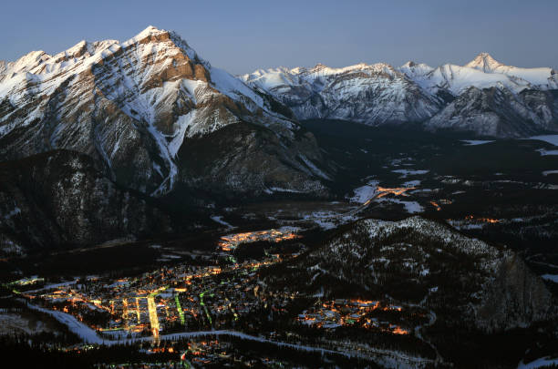 An aerial view of Banff, Alberta from Sulphur Mountain. This long exposure and night image of the tourist town of Banff highlights the beauty of the Canadian Rockies. Snow is covering the nearby mountains. Closet mountain is Cascade Mountain with Fairholm Range in the distance. The bright street is Banff Avenue where many of the hotels, restaurants, and shops are located. Banff is located approximately two hours west of Calgary. 