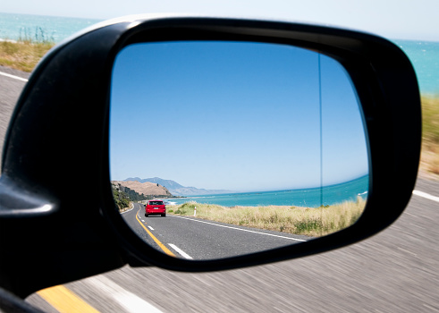 A car reflected in a wing mirror along a scenic section of State Highway 1, north of Kaikoura on New Zealand's South Island.