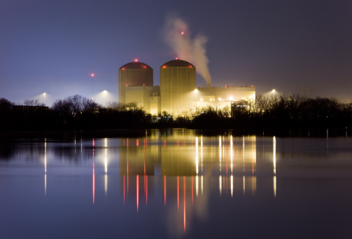 A large nuclear power facility photographed at night with light and tower reflections in the water.