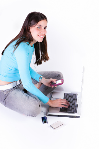 Young woman using laptop, listening music on a mp3 music player and chatting on a cellphone.